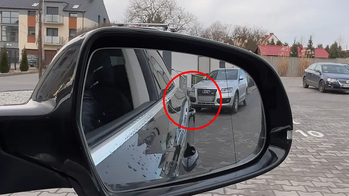 Widok w bocznym lusterku pokazujący klamkę samochodu zrównaną z pojazdem za nim