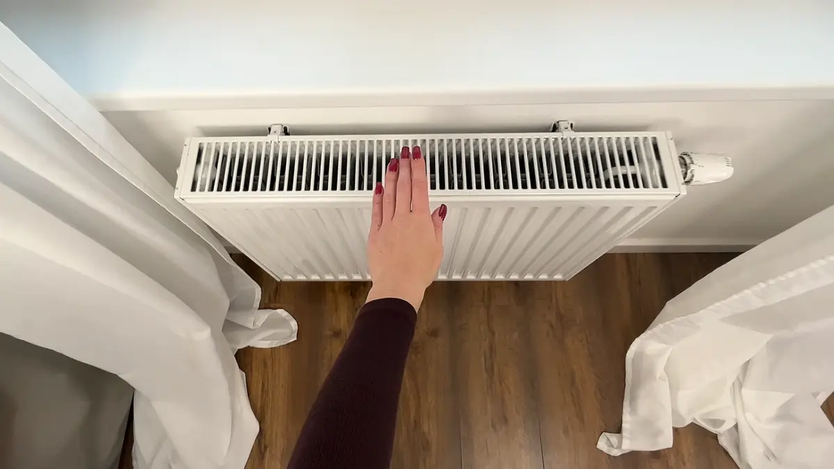Sprawdzanie dłonią temperatury na górze grzejnika, co pomaga zdiagnozować jego zapowietrzenie