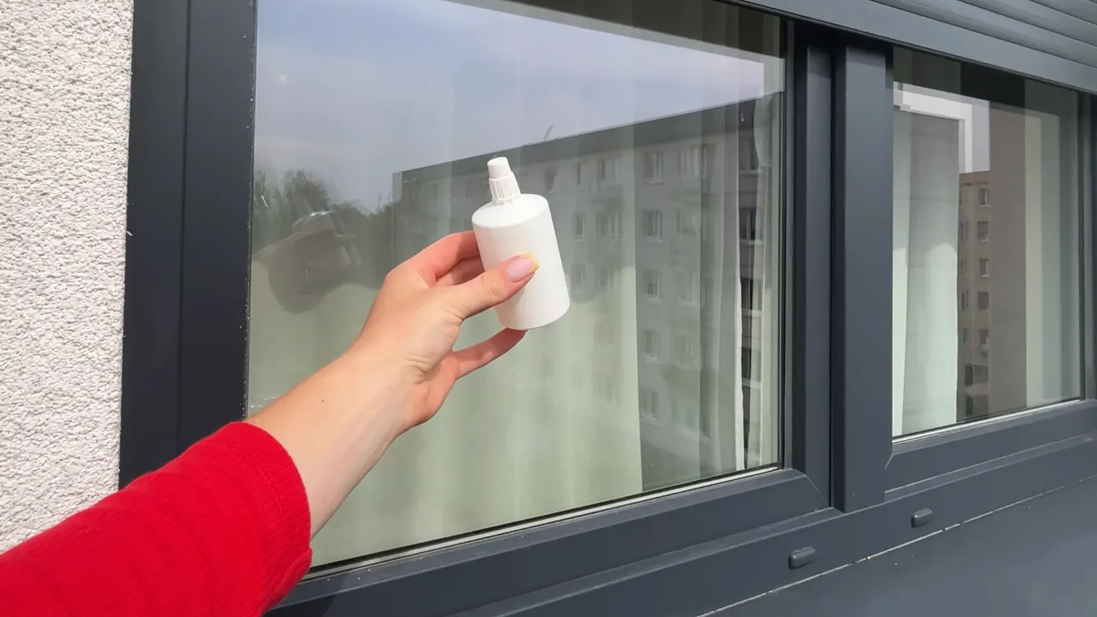 Osoba trzymająca apteczną buteleczkę z gliceryną na tle szyby w szarej ramie okiennej