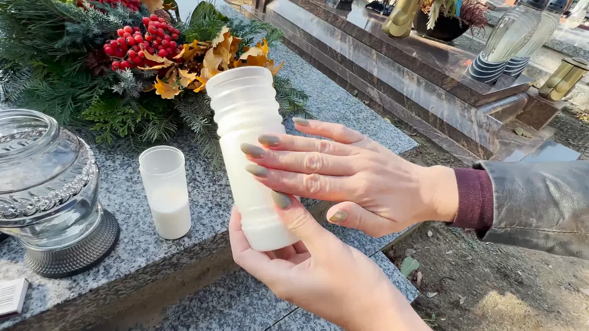 Zbliżenie na dłonie trzymające schłodzony wkład do znicza na nagrobku przed jego zapaleniem
