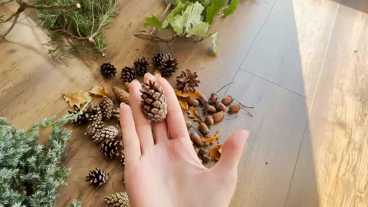 Trzymanie szyszki w dłoni na tle naturalnych leśnych ozdób na stroik